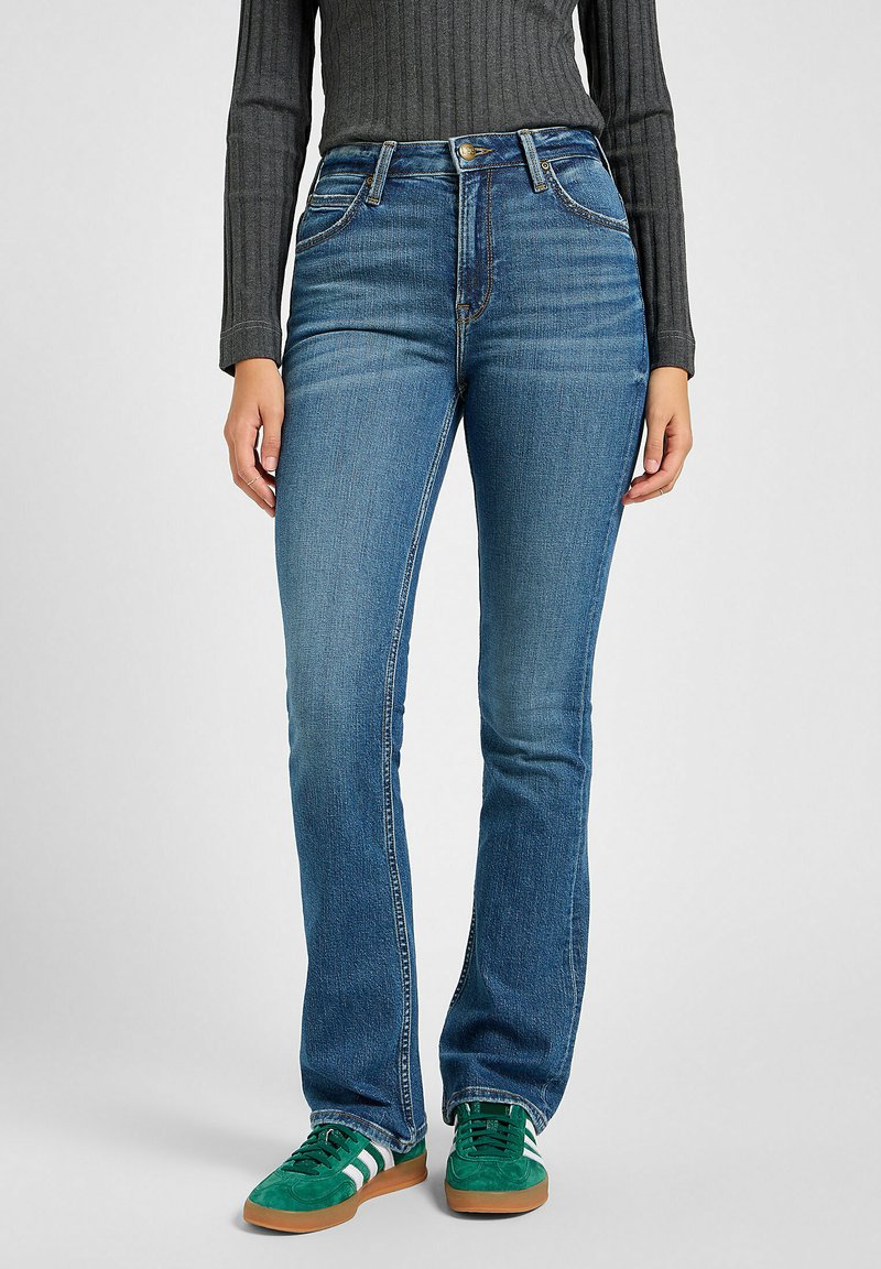 Blå denimjeans med slim fit, medelhög midja, fem fickor och subtila slitningar. Matchas med gröna sneakers och en grå ribbad topp.