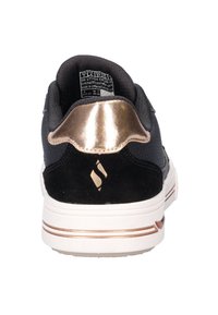 Zwarte en gouden sneaker gezien vanaf de achterkant, met het maattag binnenin en een witte zool met gouden strepen.