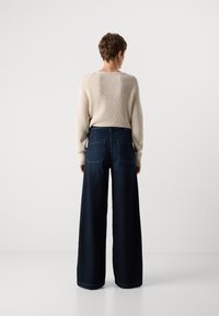 Suéter de punto beige y pantalones de mezclilla oscuros de pierna ancha de alta cintura, con bolsillos traseros y una textura suave, vistos desde la parte de atrás.