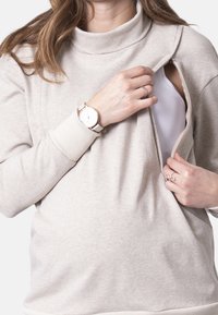 Jasnoszary, długi sweter z długim rękawem i wysokim kołnierzem. Posiada zamek błyskawiczny z boku oraz miękką fakturę. Zdobiony cienkim prążkowanym mankietem.