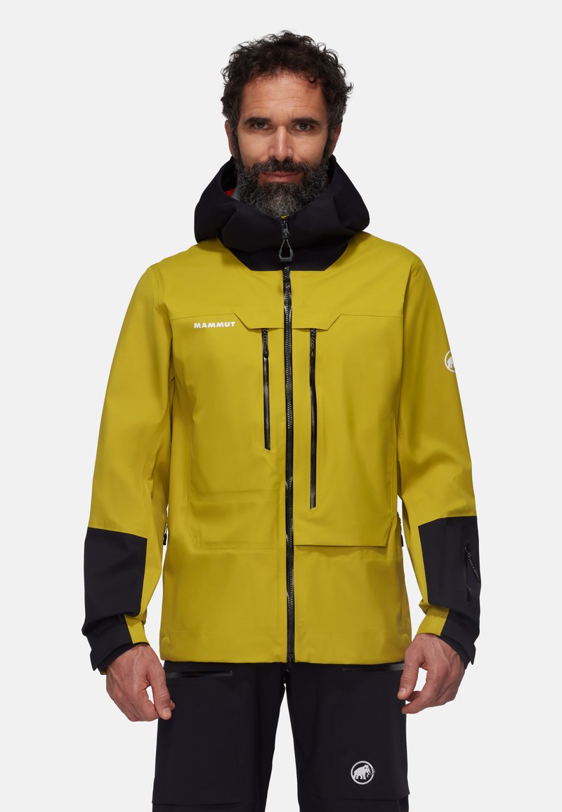Giacca impermeabile gialla con accenti neri, caratterizzata da un colletto alto, tasche con zip e cappuccio regolabile. Tessuto resistente con una consistenza liscia.