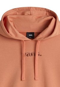 Primer plano de una sudadera Vans color melocotón con cordones y un logo bordado en el pecho, etiqueta de talla pequeña dentro de la capucha.