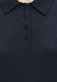 Polo en maille bleu marine foncé avec un col et quatre boutons noirs sur la patte de devant.