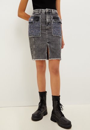 Jupe en denim gris avec des poches avant à motif chevrons, un ourlet effiloché et une fente à l'avant, associée à des bottes de combat noires à lacets.