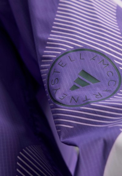 Tela morada con rayas diagonales y un logo circular. El logo contiene texto y un ícono de tres rayas, indicando la identidad de la marca.