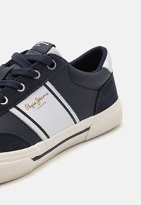 Sötétkék sneaker, fehér részletekkel és velúrváltozattal. Arany "Pepe Jeans" logóval és fehér csíkkal a sivégén.