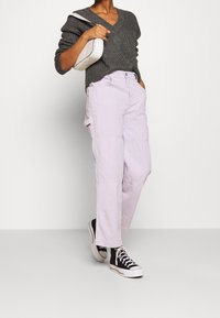 Pantaloni cargo di un lilla chiaro con tasche a toppa, abbinati a un maglione grigio scuro a scollo a V e sneaker alte nere. Accentato da un tessuto in maglia testurizzato.