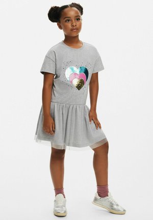 Grå klänning med en t-shirt överdel och ett hjärttryck gjort av paljetter i blått, rosa och guld, samt en glittrig tyllkjol.