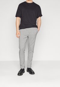 Šedé kárované kalhoty s úzkým střihem a plochým předním dílem, kombinované s černým tričkem s krátkým rukávem a černými mokasínami. Hladká textura látky.