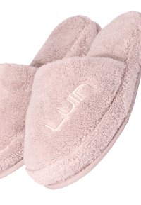 Light pink slippers made of soft, textured fabric with a plush finish. Features a stitched logo and broad open-toe design.