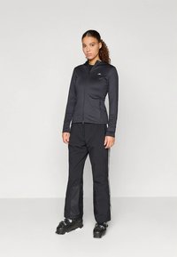 Black athletic jacket with zip closure and hood, paired with black pants featuring side stripes and boots, designed for outdoor activity.