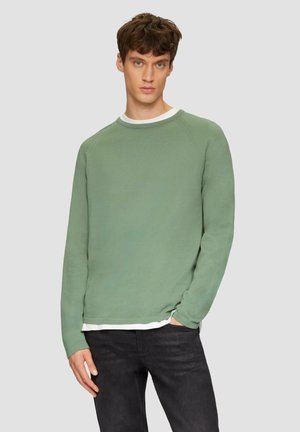 Groene crewneck sweatshirt met lange mouwen, gestructureerde stof, ontspannen fit en een gelaagd wit shirt dat zichtbaar is aan de onderkant. Draag met zwarte jeans.
