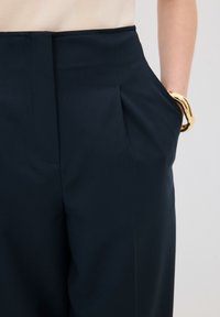 Námořnické kalhoty s elegantním vzhledem, postranními kapsami a šikmými sklady v pase. Doplněné velkým zlatým náramkem.