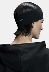 Diadema elástica negra con el logo "ON RUNNING". Textura suave, diseñada para ajustarse perfectamente. Se lleva con una prenda con capucha negra.