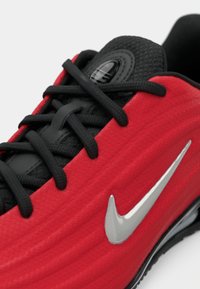 Κοντινό πλάνο κόκκινου αθλητικού παπουτσιού με μαύρα κορδόνια, μαύρη γλώσσα και ασημί λογότυπο Nike swoosh στο πλάι.