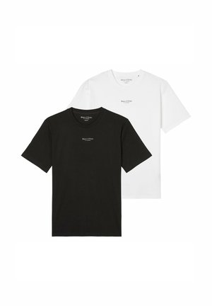 Mann trägt ein schwarzes Marc O’Polo T-Shirt mit beigen Hosen, steht mit entspannten Armen an den Seiten.