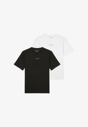 Uomo che indossa una t-shirt nera Marc O’Polo con pantaloni beige, in piedi con le braccia rilassate ai lati.