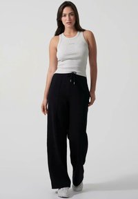Hallide ribidega tank top väikese logoga ja mustad laiad püksid stringiga, koos valgete spordijalatsitega.