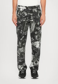 Los pantalones estampados en blanco y negro presentan intrincados diseños florales y ornamentales. El material es denim, con un corte relajado. Estilizados con zapatillas negras.