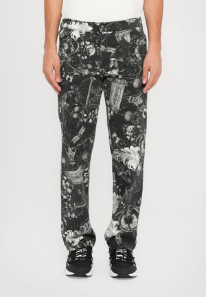 Bukser med sort-hvidt mønster har indviklede blomster- og ornamentale designs. Materialet er denim, med en afslappet pasform. Stylet med sorte sneakers.