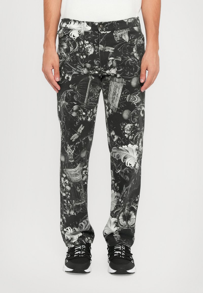 Los pantalones estampados en blanco y negro presentan intrincados diseños florales y ornamentales. El material es denim, con un corte relajado. Estilizados con zapatillas negras.