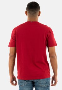 Camiseta de algodón roja con mangas cortas, cuello redondo y una pequeña etiqueta multicolor en la parte de atrás. Textura suave, ajuste casual.