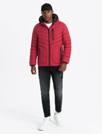 Doudoune rouge avec capuche, poches zippées et accents côtelés, associée à un jean noir déchiré et des baskets blanches.