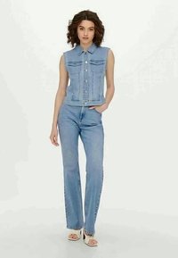 Τζιν γιλέκο με γιακά και χωρίς μανίκια, σε συνδυασμό με ελαφριά μπλε τζιν σε ίσια γραμμή. Και τα δύο κομμάτια διαθέτουν κλασικές λεπτομέρειες ραψίματος.