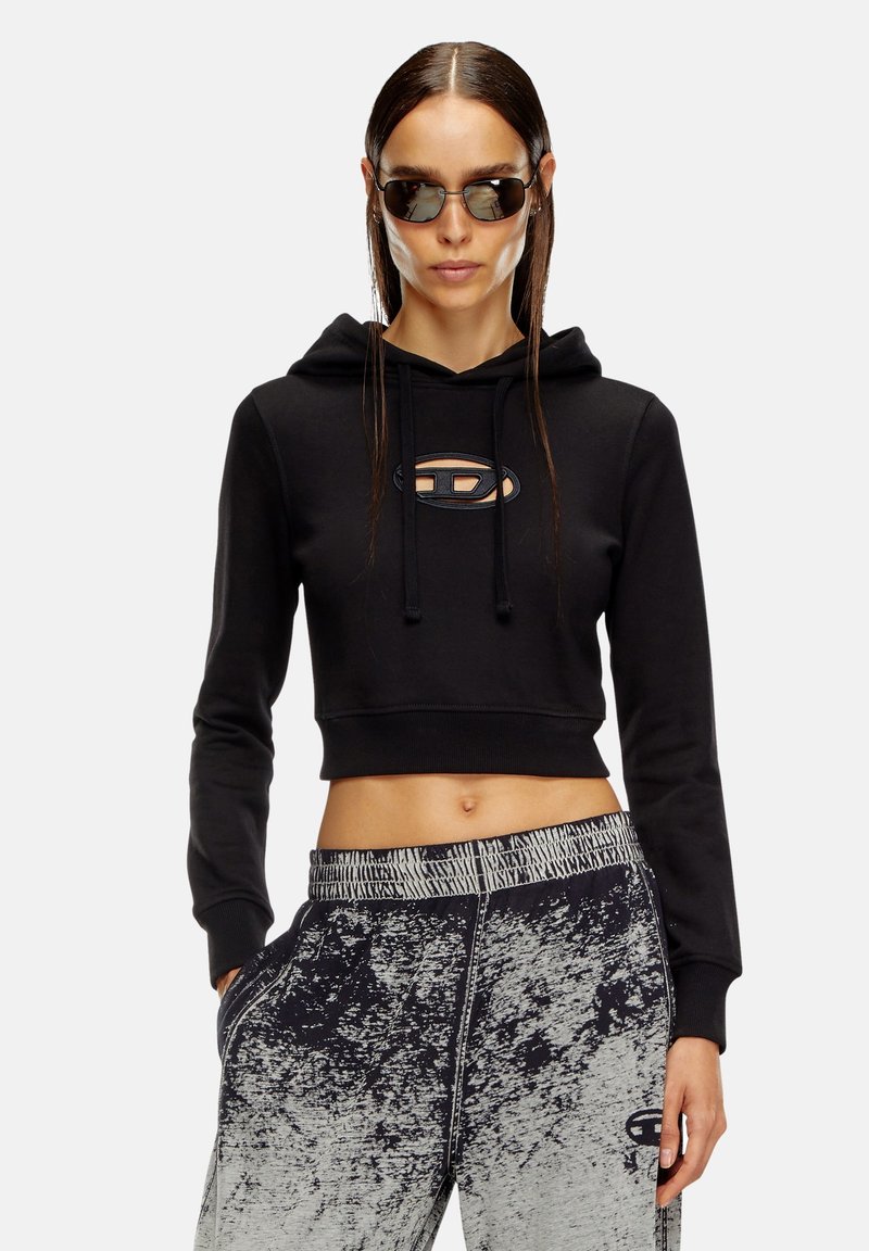 Zwarte cropped sweatshirt met trekkoorden en een cirkelvormig logo, gecombineerd met grijze en zwarte sweatpants met een patroon en een elastische tailleband.