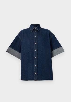 Camisa de denim escuro com mangas curtas, arregaçadas em denim mais claro. Apresenta um colarinho clássico e botões frontais. Textura suave, design casual.