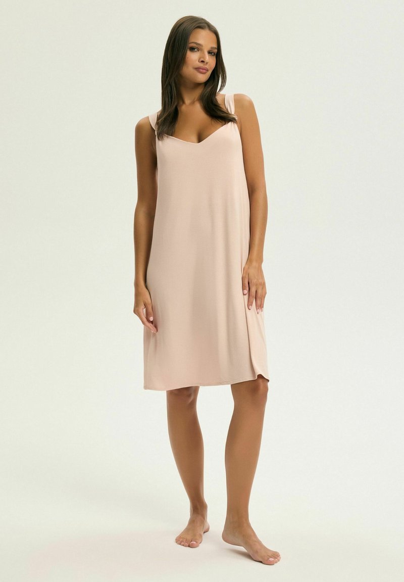 Bladoróżowa koszula nocna do kolan z dekoltem w serek i cienkimi ramiączkami, wykonana z miękkiego, gładkiego materiału. Brak widocznych wzorów lub detali metalowych.