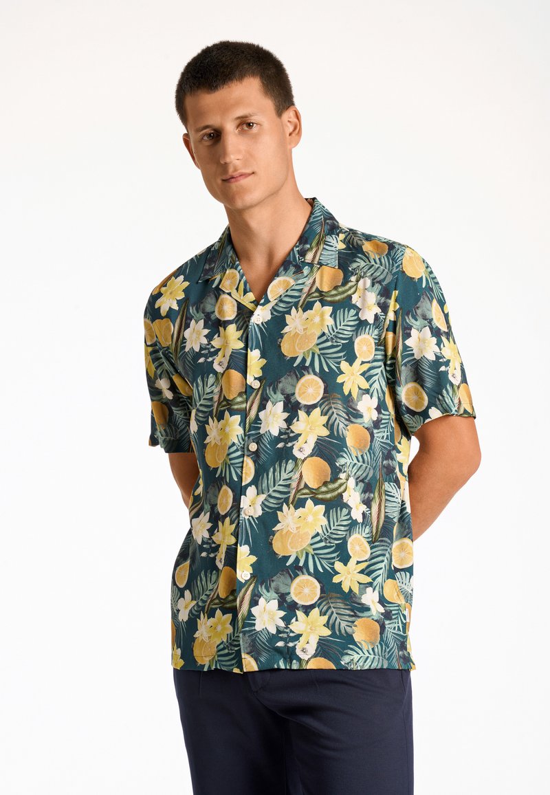 Camisa de manga corta hecha de tela ligera que presenta una base verde con patrones de cítricos amarillos y flores. Incluye un cuello con muesca y botones.