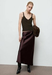 Maiou negru tricotat cu bretele subțiri, asortat cu o fustă maxi din satin burgundy. Modelul ține o poșetă pufă maro și poartă cizme negre până la gleznă.