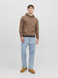 Bruine hoodie met een voorzak, gecombineerd met lichtblauwe ontspannen jeans en bruine laarzen. Eenvoudig design, zachte stof.