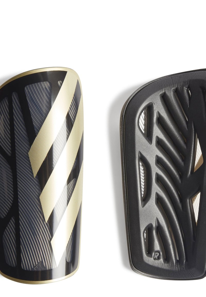 Le protezioni per le tibie da calcio nere e oro presentano una superficie testurizzata, strisce diagonali e un design curvo. Il retro mostra un motivo a coste per la ventilazione.