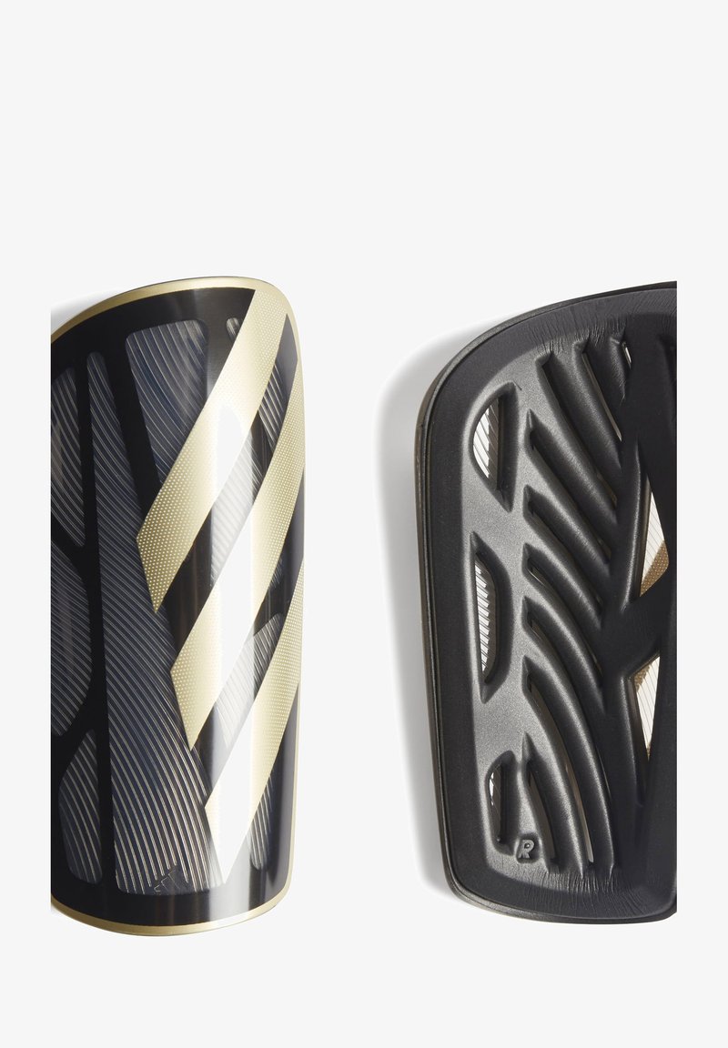 As palas de futebol em preto e dourado apresentam uma superfície texturizada, riscas diagonais e um design curvado. O verso exibe um padrão estriado para ventilação.