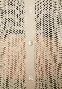 Lettstrikket cardigan med åpent mesh-design, med en gradientfarge fra krem til brun, og seks perleknapper.