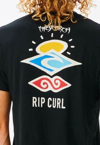 Zwarte t-shirt met kleurrijk grafisch ontwerp: blauwe golf, gele zon, rode zwirls en de tekst "RIP CURL" op de achterkant.