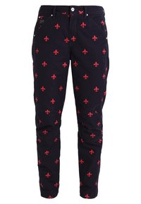 Pantalon noir avec motif fleur-de-lys rouge, poches avant, fermeture par bouton et zip, et détails cousus aux genoux.