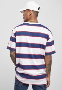 Tricou pentru bărbați cu mânecă scurtă, cu dungi orizontale bleumarin și albe, accente roșii, guler rotund și slituri pe laterale. Materialul pare a fi din bumbac.