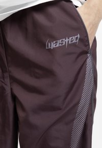 Maroon athletic pants made of lightweight fabric, featuring a logo on the thigh and a side panel with a dotted pattern in gray.