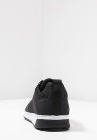 Black sneaker with mesh and synthetic materials, padded collar, white midsole, textured surface, and branding on the heel.