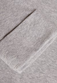 Šedá pletenina s jemnou strukturou, zakončená ohrnutým manžetovým detailem. Povrch vykazuje jemný melírovaný vzor.