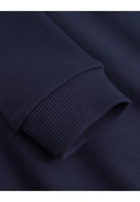 Marineblå sweatshirtarm med ribbestrikket mansjett, med en jevn tekstur og rene sømdetaljer, som fremhever det enkle designet.