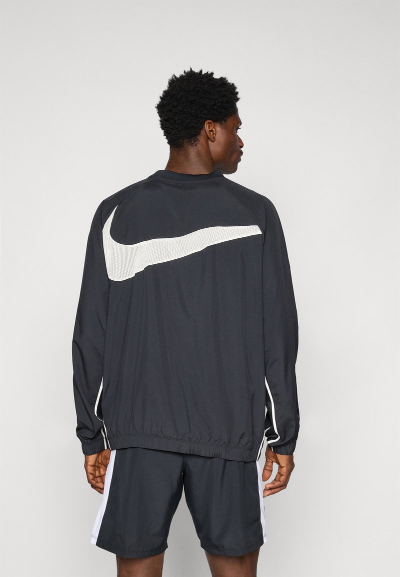 Zwarte Nike-jack met wit logo, met elastische manchetten en zoom, gecombineerd met zwarte shorts. Glad textuur, sportieve pasvorm.