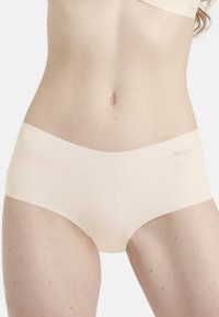 Beige saumattomat hipster-alushousut, joissa on sileä pinta ja leveä vyötärö, ja jotka esittelevät hienovaraista brändäystä edessä.