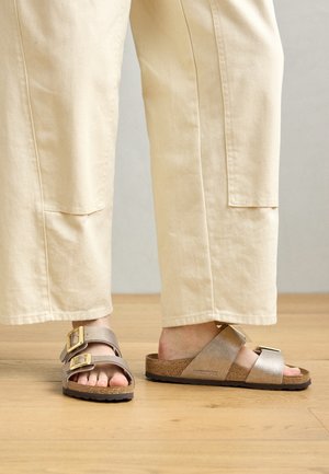 Brune kork fotsengsandaler med to brede stropper - en grå og en metallisk gull. Strukturert overflate med justerbare spenner for passform.