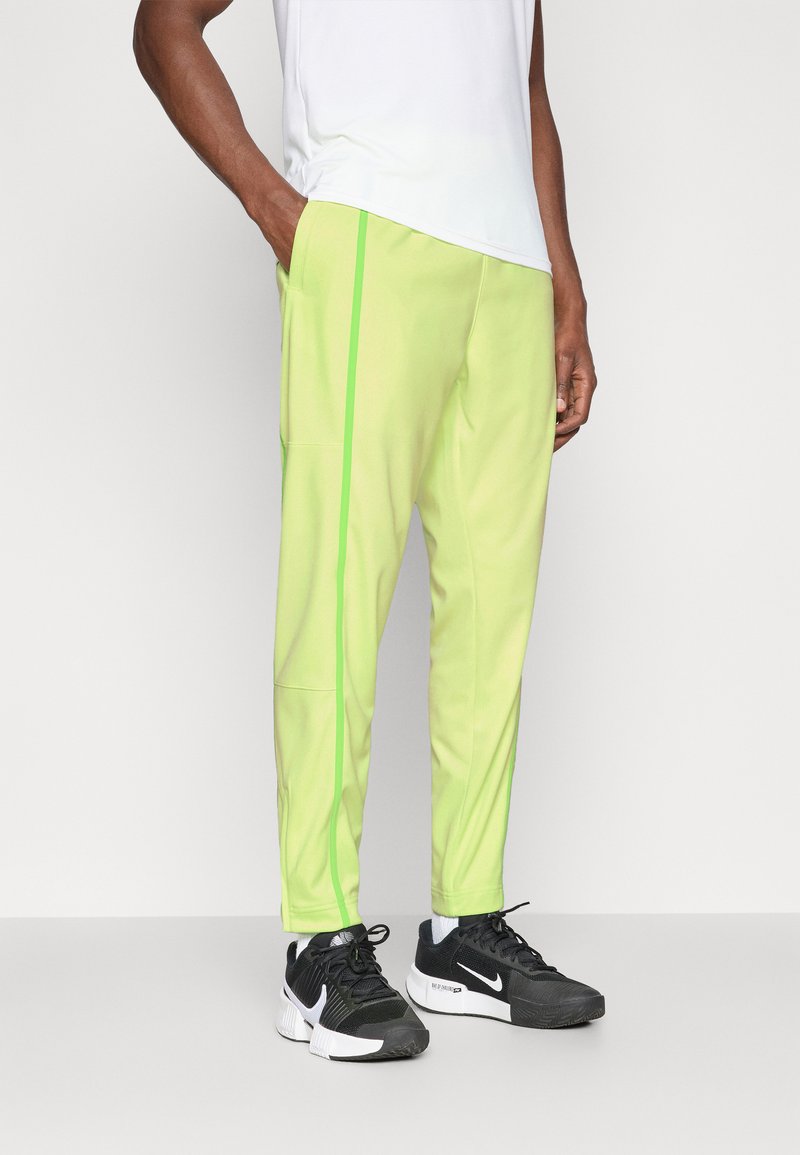 Pantalones de chándal verde claro con franjas laterales en neón verde contrastante, fabricados con una tela suave. Combinados con zapatillas deportivas negras con acentos en blanco.