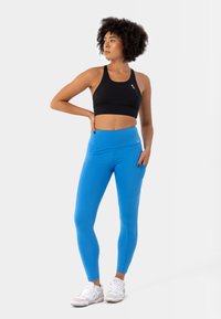 Reggiseno sportivo nero con spalline larghe e logo, abbinato a leggins alti in vita di un brillante blu con tasche laterali e una texture liscia.