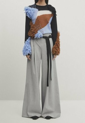 Colorful sweater with textured blue, brown, and black sections, paired with wide-leg gray trousers and a black belt, creating a layered look.